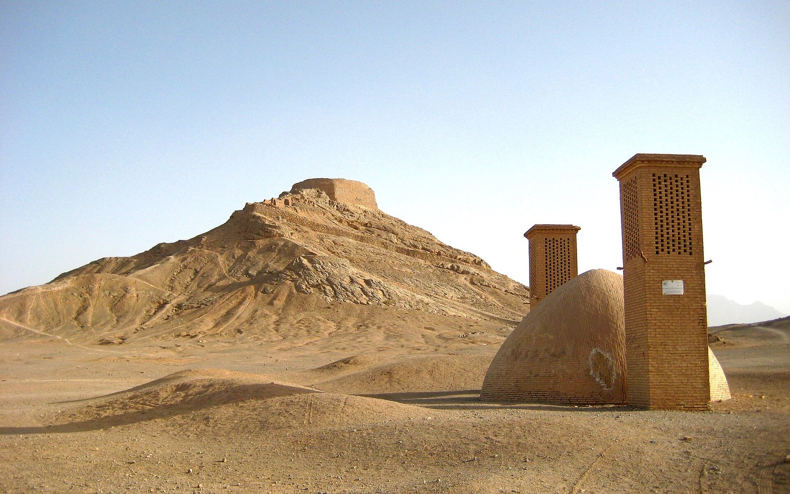 Brick windcatcher towers rise beside a domed water cistern near the Yazd towers of silence