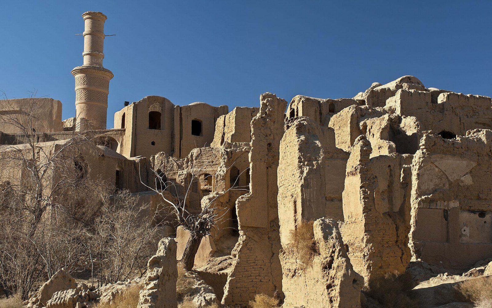 Crumbling mud-brick walls and a tall minaret rise above the abandoned old city