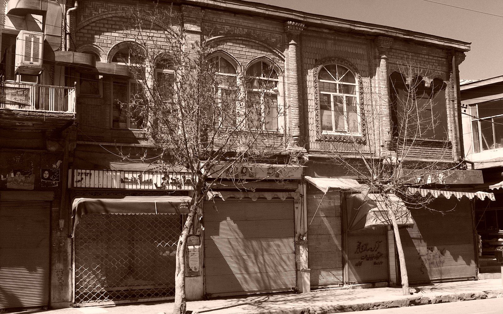 Bare trees stand before an old brick building with shuttered street-level shops