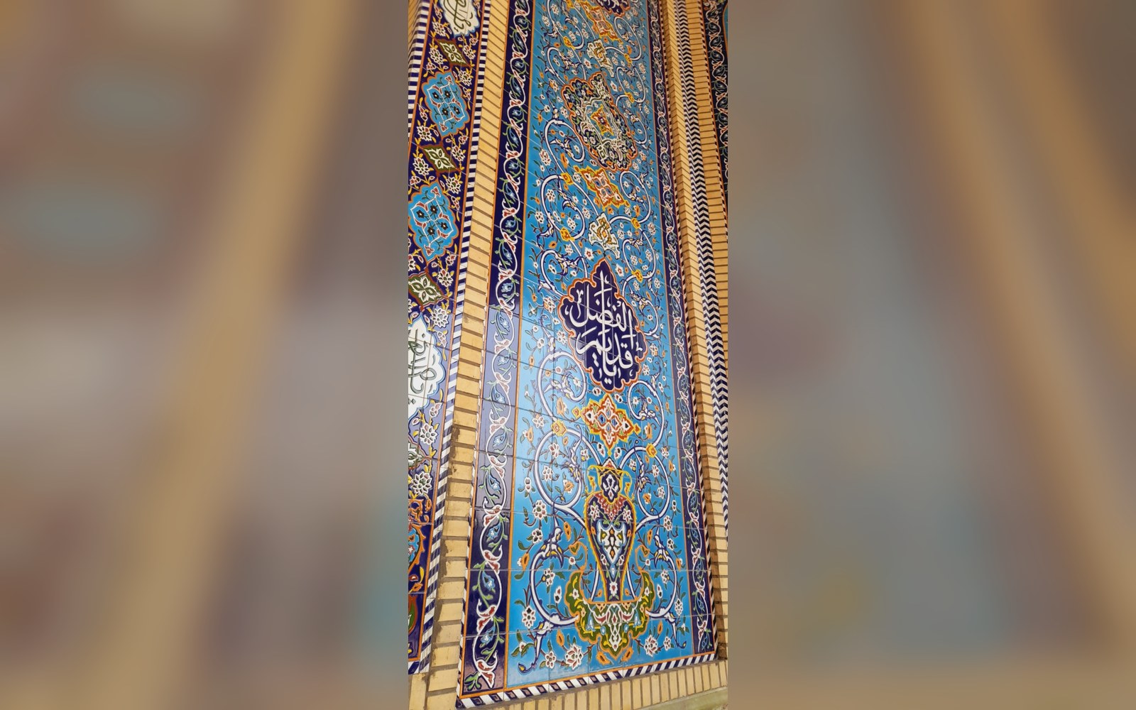 Blue mosaic tilework panel with floral patterns and Arabic calligraphy on a mosque column