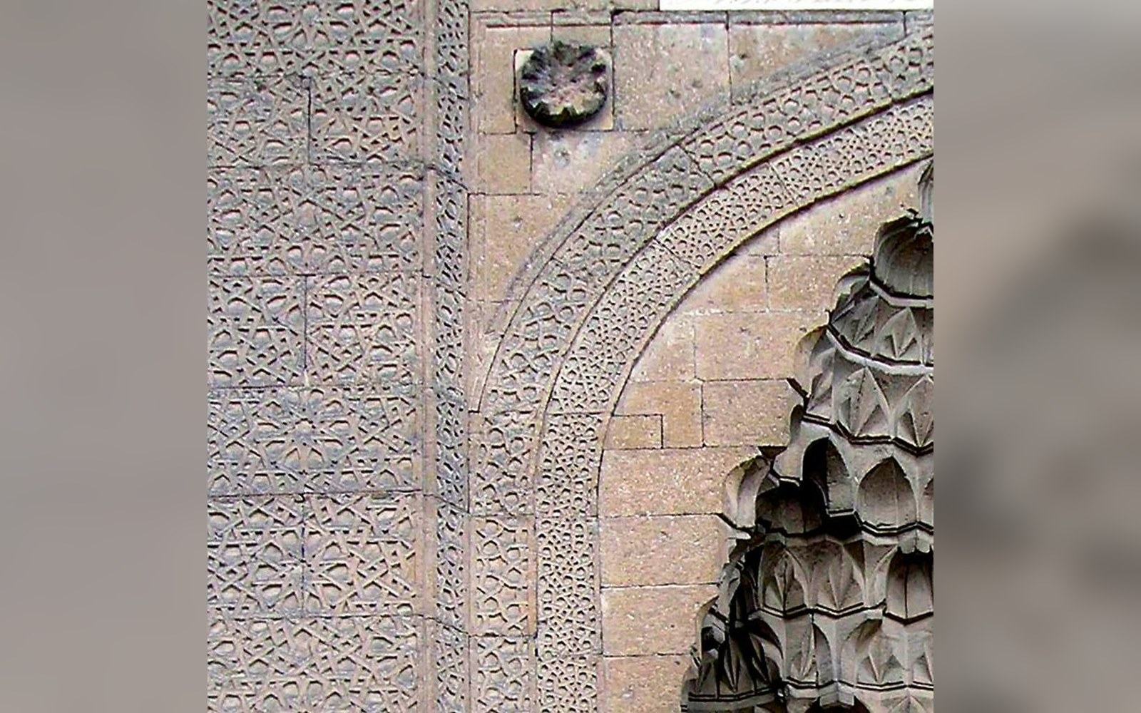 Carved stone archway with intricate geometric girih patterns and honeycomb muqarnas detailing