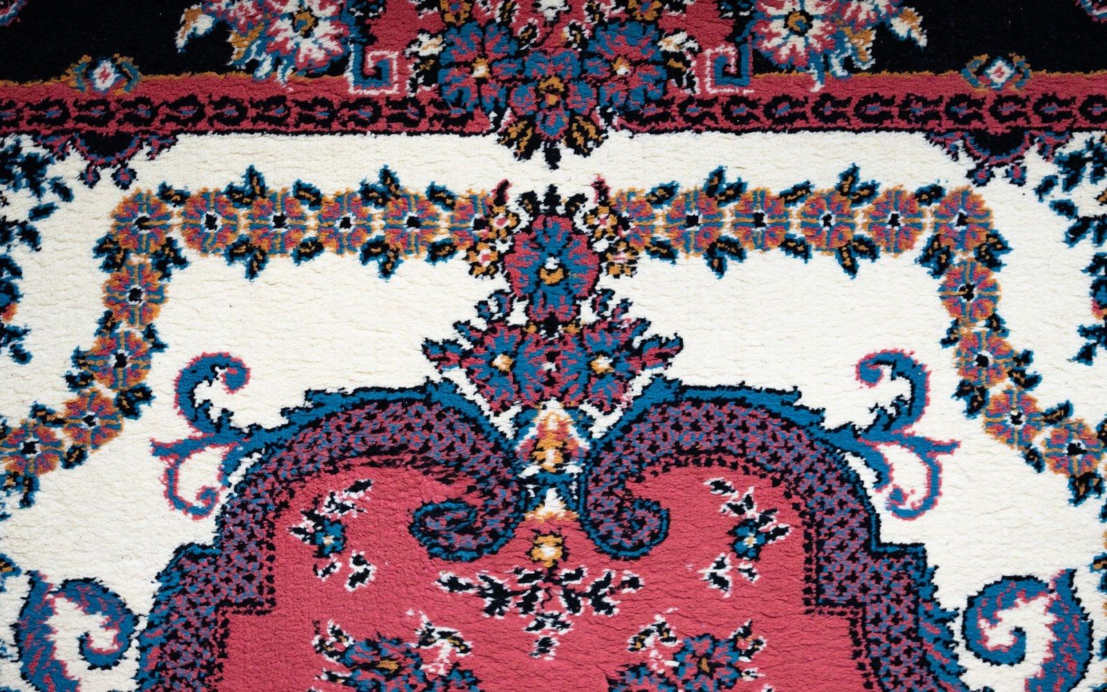 Close-up of a hand-knotted rug showing floral medallions in red, blue and cream wool