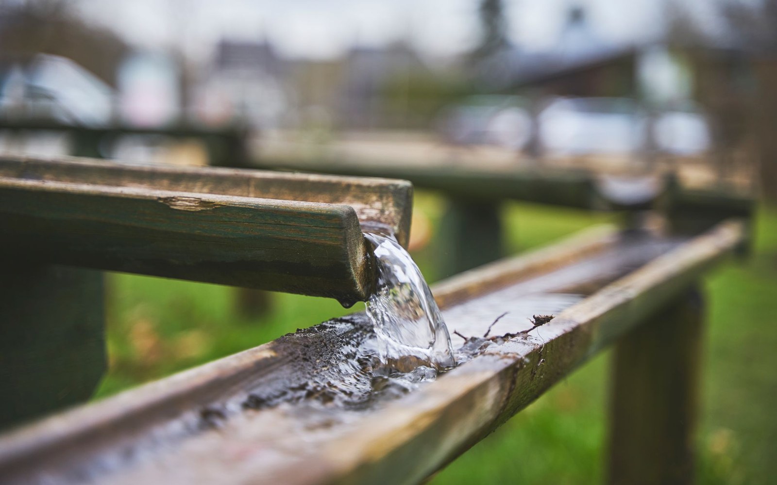 Water flows from a wooden spout into a long trough-like channel outdoors